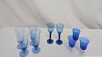 All 9 stemware glasses grouped on a white surface showing different designs and hues of blue and green in the glasses.