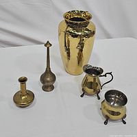 Set of five brass items on white surface: hammered vase with twisted cord tie, creamer pitcher, sugar bowl, genie bottle, incense burner.