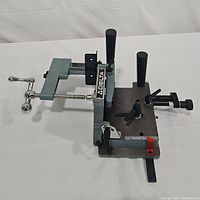 Side view of Delta tenoning jig showing chrome clamp handle, two black handles, and steel base with Delta logo.