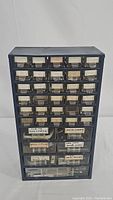 Front view of blue hardware organizer with 35 small clear drawers with white labels.