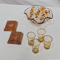 Photo showing all items in the lot including the fluted glass bowl with orange berries, four gold leaf rimmed glasses, and the two amber candlestick holders