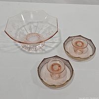 Photo showing the pink footed etched floral dish alongside two pink depression glass candlestick holders on a plain surface.