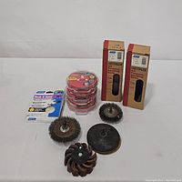 Five sanding attachments including wire brushes, flap wheel, and sanding pad along with two boxes of Norton sanding belts and a box of hook & sand 5" orbital discs