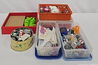 Full view of the sewing items arranged in multiple containers including thread spools, fabric patterns, scissors, and other accessories.