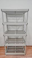 Full front view of the 5-tier white plastic shelving unit with grid shelves and black corner caps.