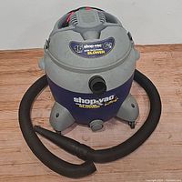 Front angled view of the 16-gallon Shop-Vac showing the body, hose attached to front, pull-out wheels, and main label.