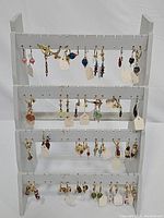 Full display of earrings arranged on a white three-tier earring stand showing a variety of styles, colors, and bead shapes.