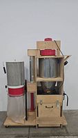 Front view of the vacuum dust collector showing motor housing, cylindrical metal filter, collection bag, and wooden frame.