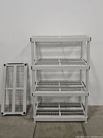 White 4-tier stackable shelving unit with extra shelf standing next to it against a white wall on floor