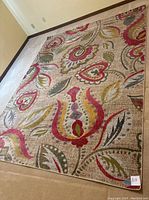 Large view of the rug laid flat showing the full multicolored floral and paisley design with warm tones and textured background.