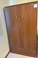 Full front view of a wood veneer standalone wardrobe with two doors and two drawers at the bottom, showing wood grain finish and wooden handles.
