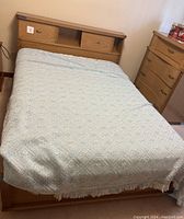 Assembled bed with headboard, mattress covered by blue and white blanket, footboard visible