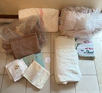 Full view of all bedding items including folded comforter, quilt, pillow shams, blanket, mattress protector, pillowcases, sheets in packaging, and white sheets.