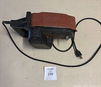 Black & Decker belt sander placed on a flat surface with visible sanding belt and power cord.