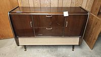 Front view of mid-century wooden cabinet with integral record player and speakers, showing side doors, drawers, and woven mesh speaker cover.