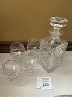 Photo showing square glass whiskey decanter and four etched brandy glasses arranged together.
