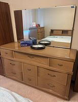 Solid wood 9-drawer dresser with mirror on top reflecting room, dresser has metal handles and natural oak finish.