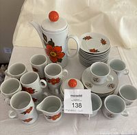 Front view of Winterling Bavaria espresso pot with orange flower design, matching cups and saucers, sugar bowl and creamer arranged on a white cloth.