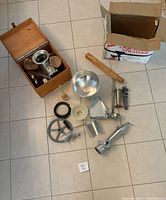 Full overview of food grinder, strainer parts, wooden box, and accessories on floor from above.