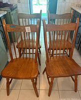 Four solid wooden dining chairs with spindle backs arranged in kitchen setting, showing front and angled views.