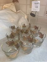 Eight low ball drinking glasses with decorative gold and green leaf motifs arranged in two rows.