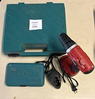 Makita hammer drill in teal carrying case, separate small Makita drill bit case, Skil 18V battery hammer drill, and charger laid out on table.