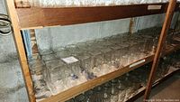 Wooden shelf holding approximately 20 clear glass mason jars, no lids, arranged in rows, need cleaning.
