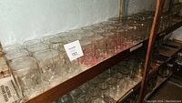 Photo showing multiple rows of clear square mason jars on a basement shelf, all without lids, with some dust and dirt visible.