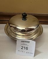 Silver plated muffin warming plate with domed lid and black knob handle shown from one angle.