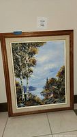 Full view of the framed oil painting showing landscape with birch trees, lake, cabin, birds and clouds.