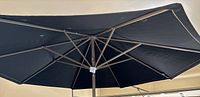 View of the underside of large black fabric umbrella canopy with metal ribs and central pole.
