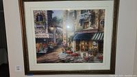 Front view showing framed print of outdoor European street café scene with flower stalls and stone buildings