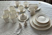 Full set displayed on quilted white surface shows plates in three sizes, teacups with saucers, four mugs, gravy boat with matching underplate, creamer, covered sugar bowl, and salt and pepper shakers.