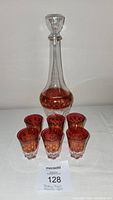 Overall view of ruby red glass decanter and six matching shot glasses on white surface