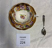 Top view of the Royal Albert teacup with saucer and Oneida teaspoon displayed on white fabric.