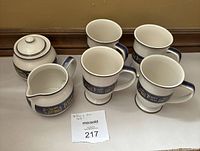 Full set view showing four tea cups, sugar bowl with lid, and creamer with Tetley branding, placed on a white surface against a beige background.
