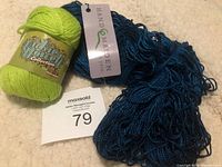 Two skeins of yarn, lime green and blue, with brand tags visible and lot number 79 noted.