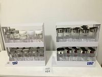 Two white swivel racks with two tiers each, holding glass spice jars with a mix of metal and plastic lids. Spice jars are labeled.