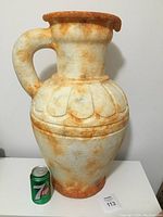 Front view of large urn vase next to 7UP can for scale; textured cream and rust finish, handle on left.