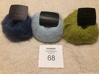 Three balls of Drops Symphony yarn in deep blue, light blue, and green on a cream background with labels visible