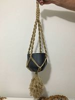 30 inch macrame plant holder with large decorative tassel at bottom, holding a dark gray pot.