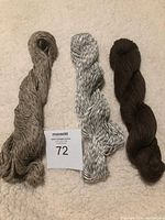 Three skeins of artisan yarn in neutral and brown tones laid out on a fabric surface, arranged side by side.