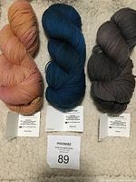 Three skeins of Artizan So-Soft Sock yarn in peach/orange, deep blue, and grey-brown colors displayed on fabric background with labels visible.