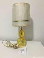 Front view of amber coloured lamp showing plastic/lucite body and white textured shade. Lamp cord with inline switch is visible.