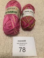 Photo showing two balls of yarn on a beige surface with lot number card in front