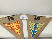 Two paper star lanterns in original flat cardboard packaging, one with red and yellow pattern and one with blue and yellow pattern.