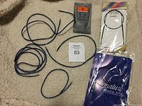 Lot of round knitting needle cables and tips laid out on fabric background, some in original packaging including Signature Needle Arts and KnitPro.