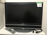 Front view of Sony 26-inch HD TV with remote and power cord placed in front and power cord coiled beside it.