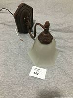 Rusty brown metal wall light with frosted glass shade shown from side angle giving a clear view of the base and arm