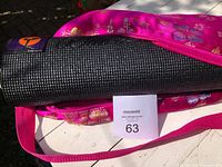 Black textured Wai Lana yoga mat partially rolled, placed on pink floral carrying case, showing texture and partial logo patch.
